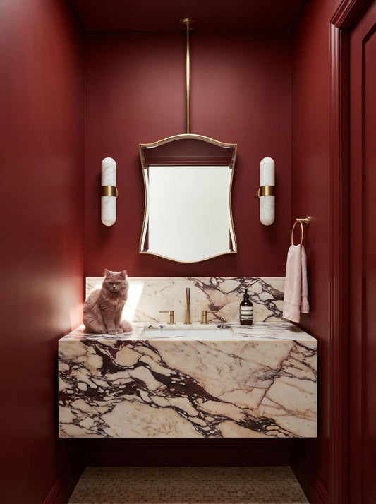 Curved brass hanging mirror in deep red luxury powder room