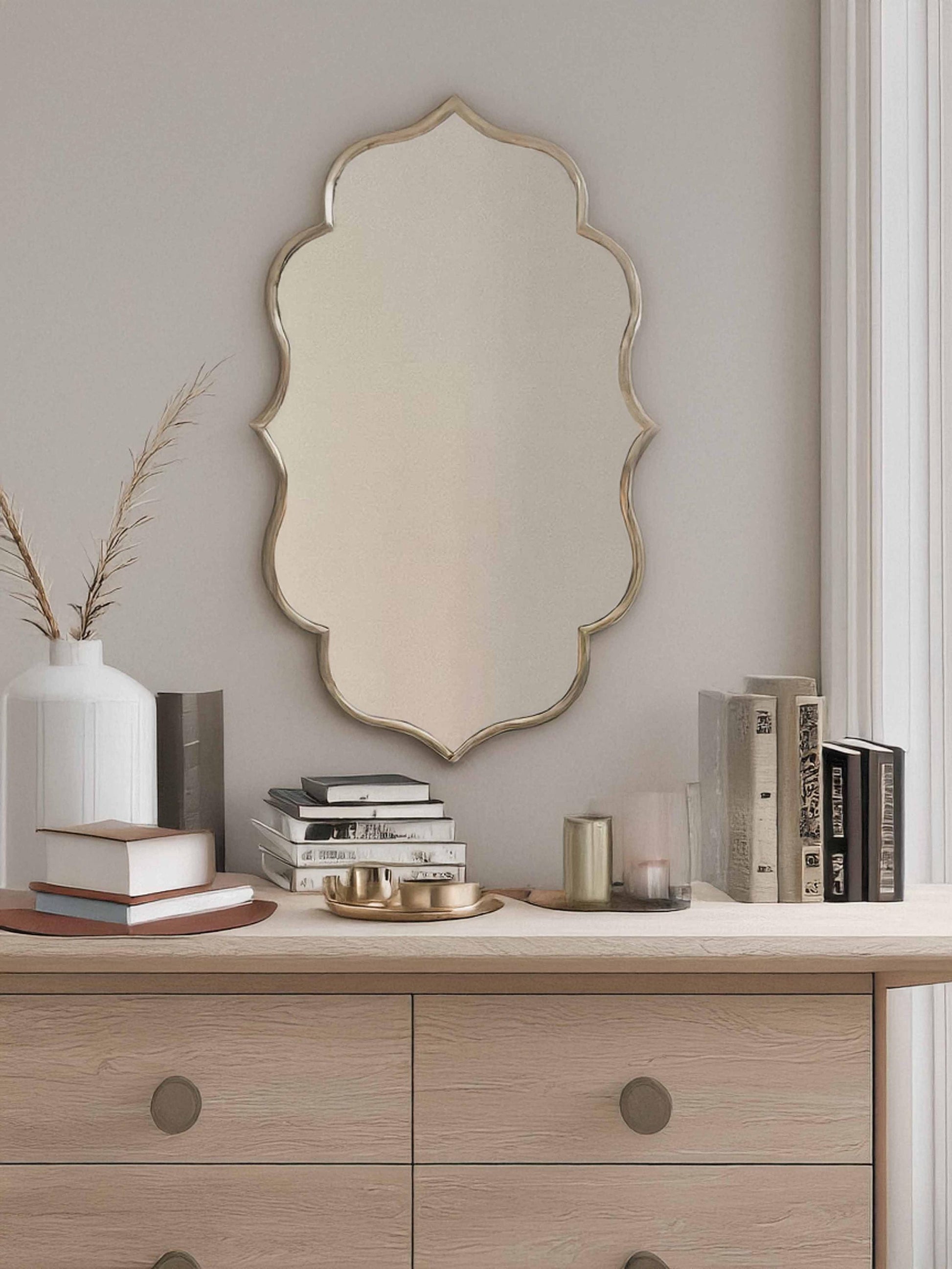 Flower brass mirror above a wooden dresser with decor.