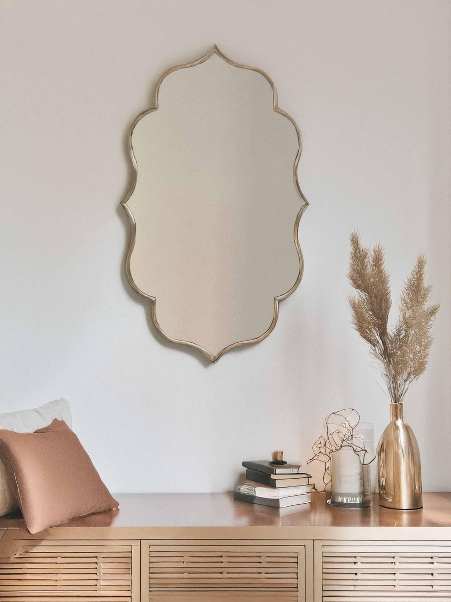 Wavy brass mirror above rattan console with decor.