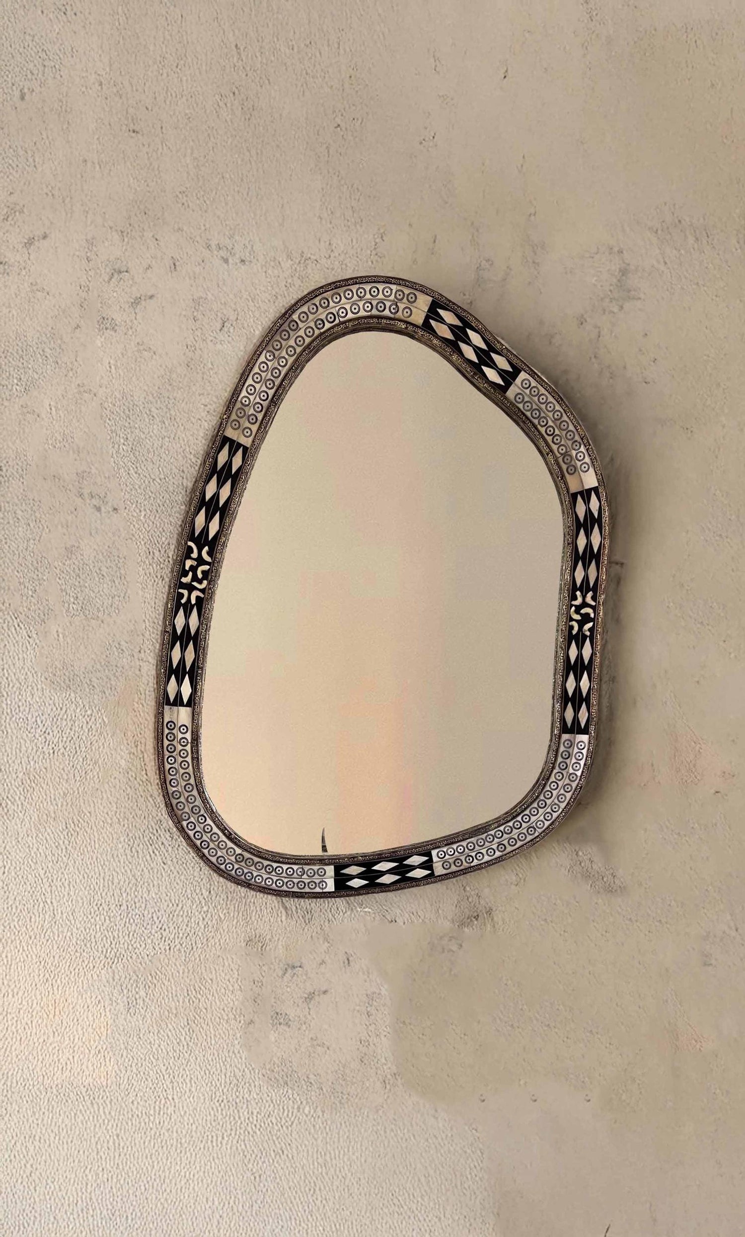 Organic-shaped bone inlay mirror with intricate black and white tribal patterns mounted on a textured beige wall
