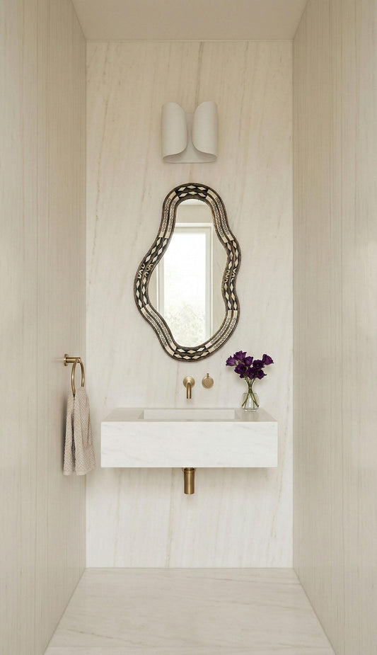 Freeform bone brass mirror above white marble floating vanity