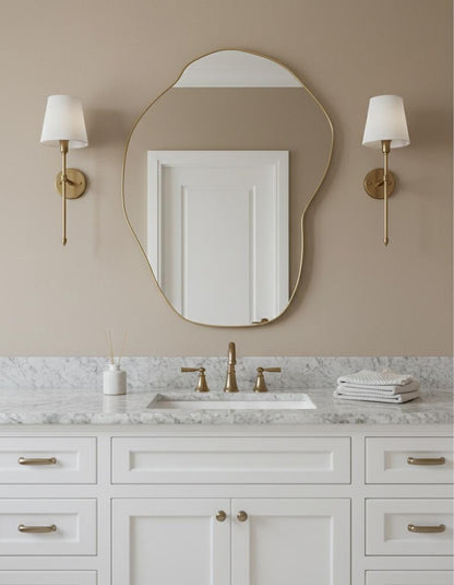 Irregular brass wall mirror above bathroom vanity with gold fixtures