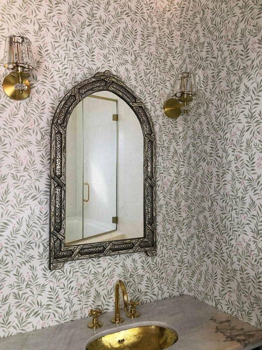 Arched bone inlay mirror above brass sink in patterned bathroom wall