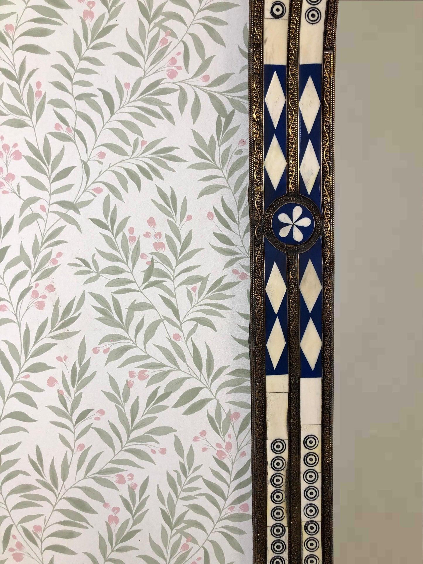 Close-up of blue and ivory inlay mirror frame with floral wallpaper.