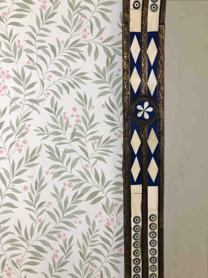 Close-up of blue and ivory inlay mirror frame with floral wallpaper.