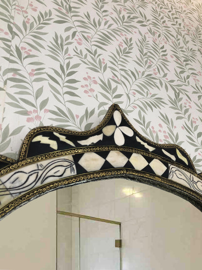 Top detail of arched bone inlay mirror with ornate black and white floral design.