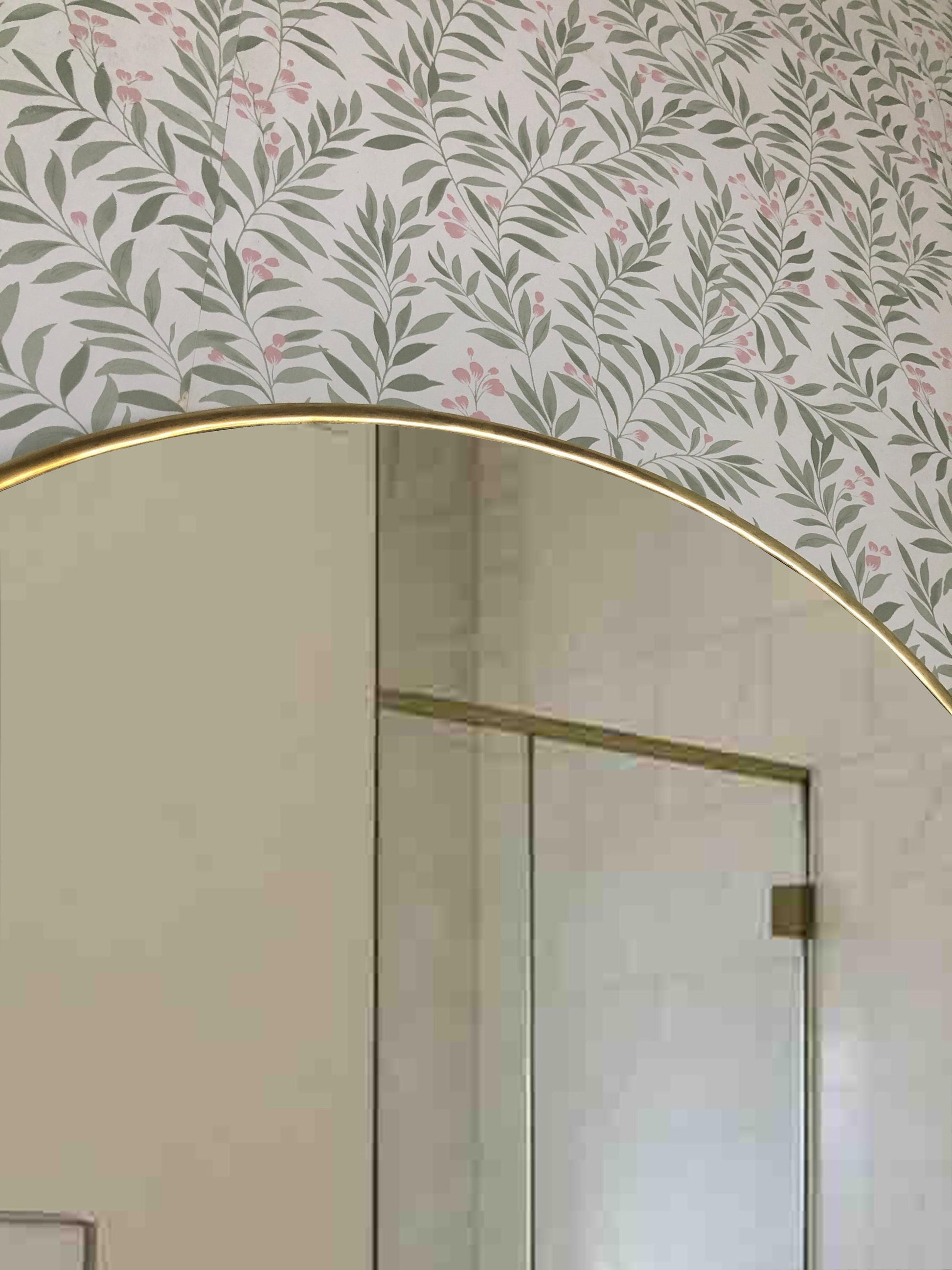Top curve of brass arch mirror against floral wallpaper.