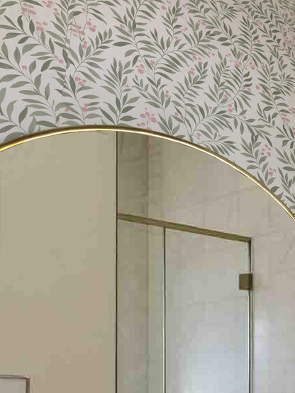 Top curve of brass arch mirror against floral wallpaper.