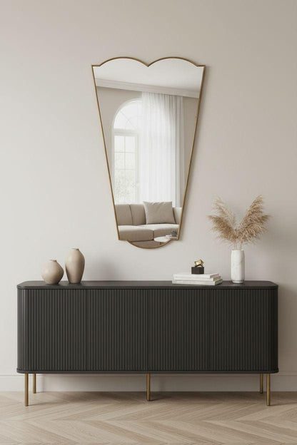 Asymmetrical tapered brass mirror above black sideboard