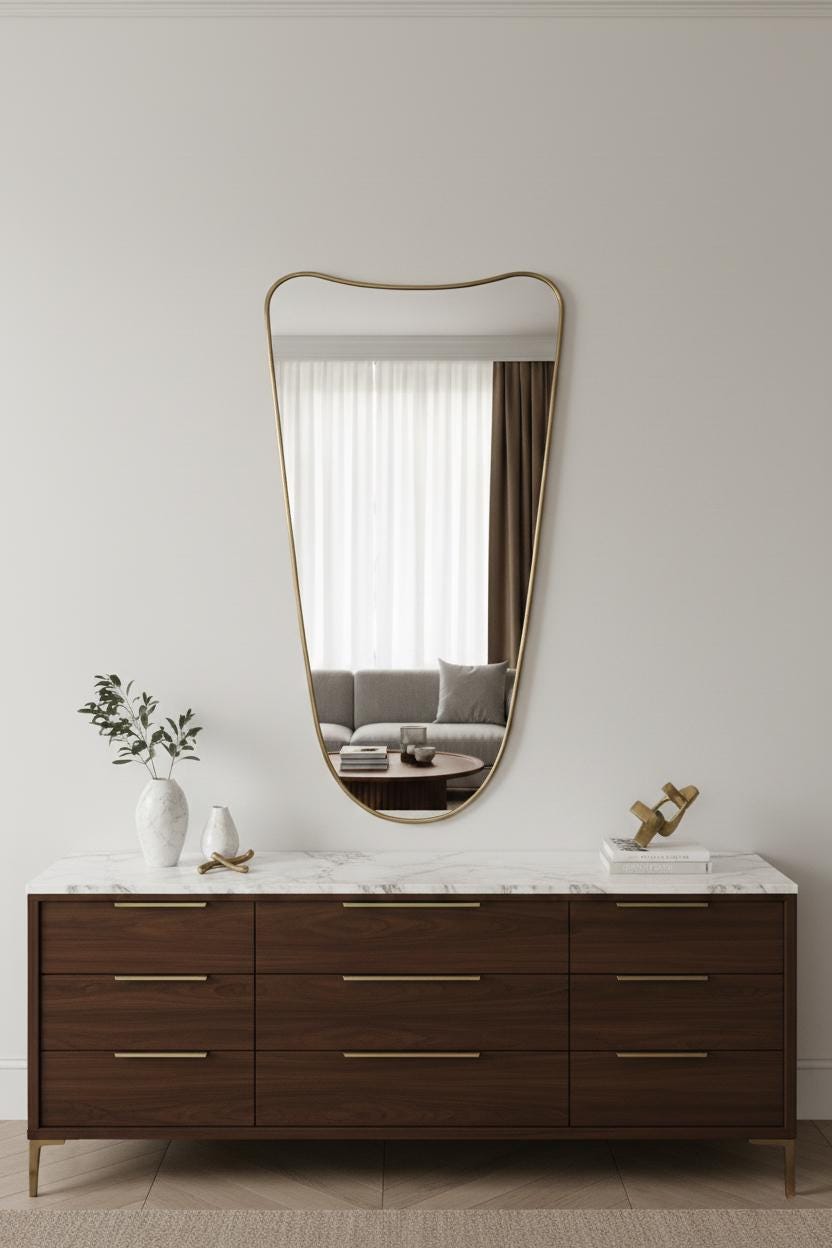 Brass asymmetrical mirror mounted above a dark wood dresser with marble top.
