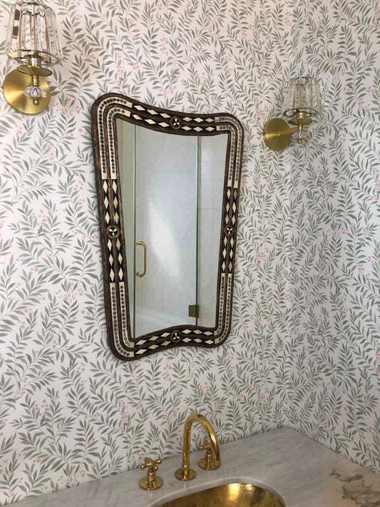 Mirror with brass faucet and floral wallpaper.