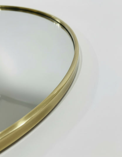 a close-up view of a round mirror with a gold-colored frame, placed on a white surface.