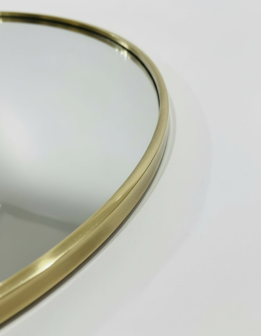 a close-up view of a round mirror with a gold-colored frame, placed on a white surface.