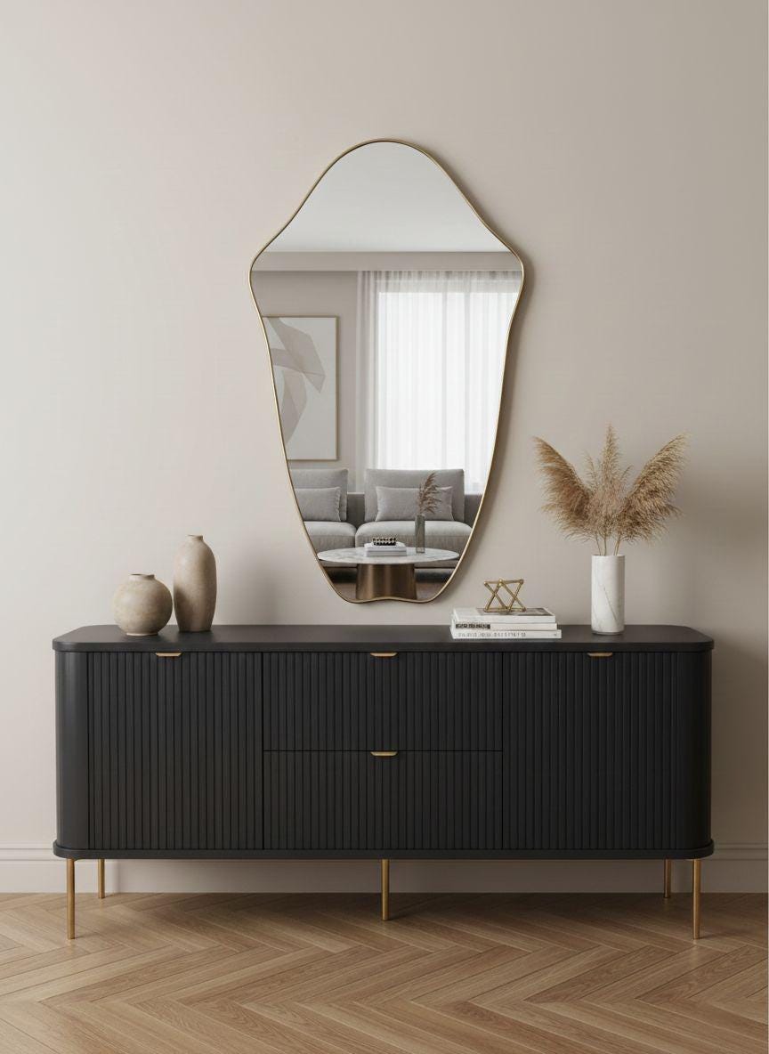 Organic curved brass mirror styled above black sideboard