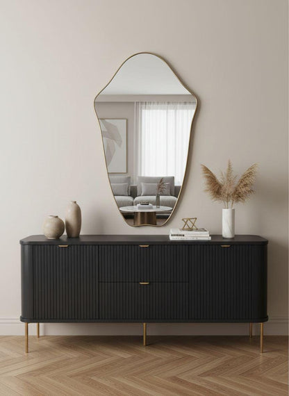 Organic curved brass mirror styled above black sideboard
