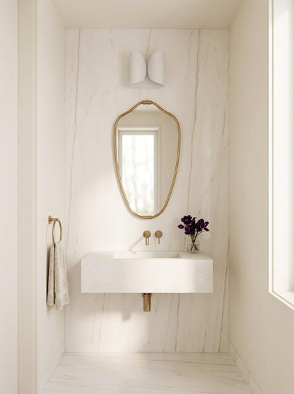 Curved gold mirror in minimalist white marble bathroom setting