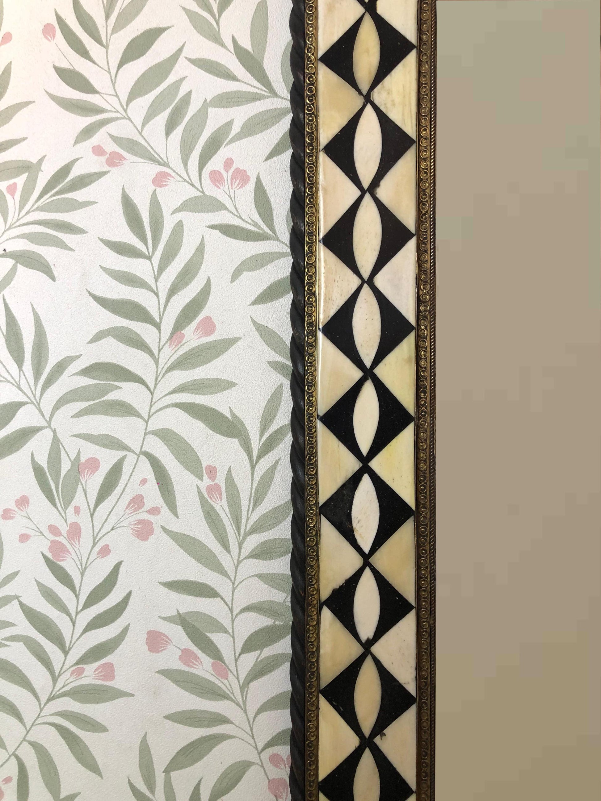 Side view of the mirror showing geometric inlay and floral wallpaper background.