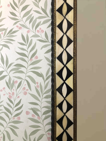 Side view of the mirror showing geometric inlay and floral wallpaper background.