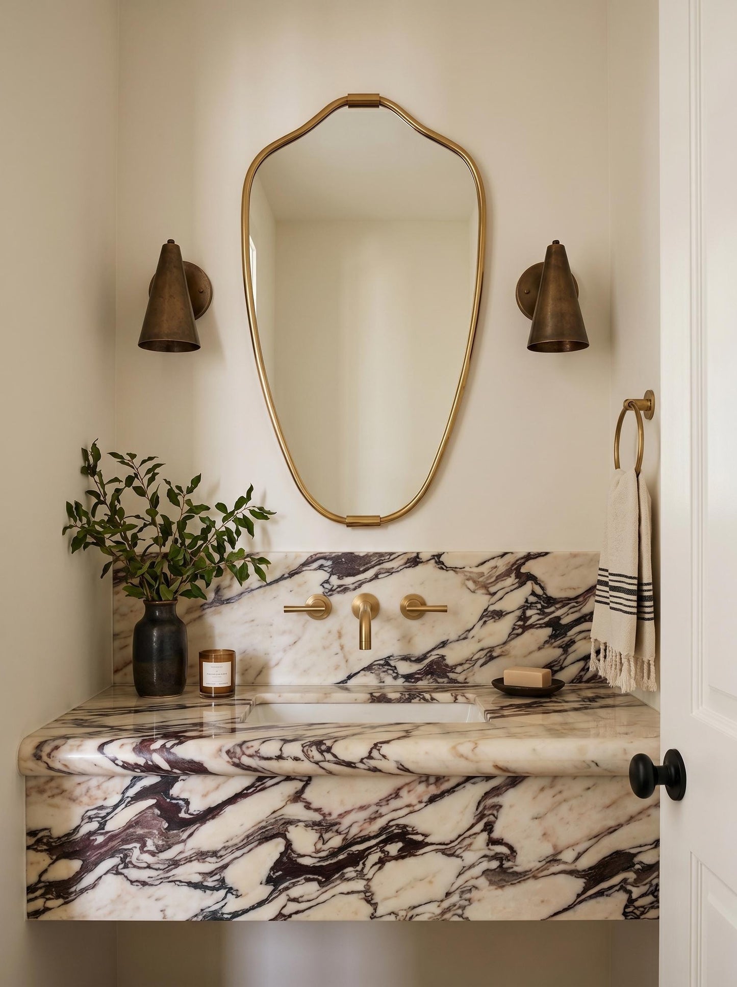 Organic brass mirror above marble vanity with wall sconces