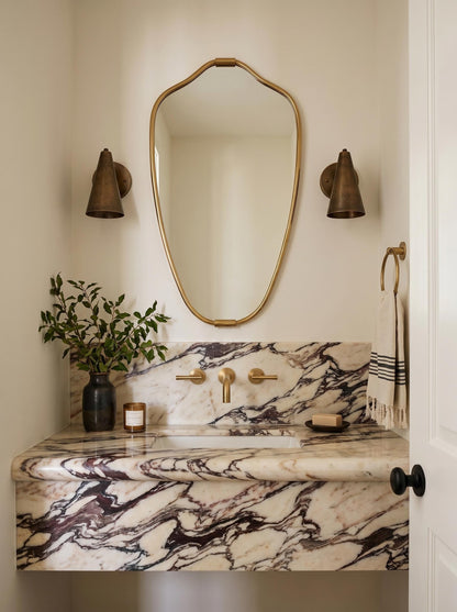 Organic brass mirror above marble vanity with wall sconces
