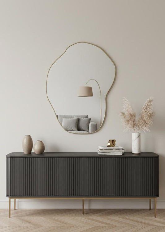 Freeform brass wall mirror styled above modern sideboard