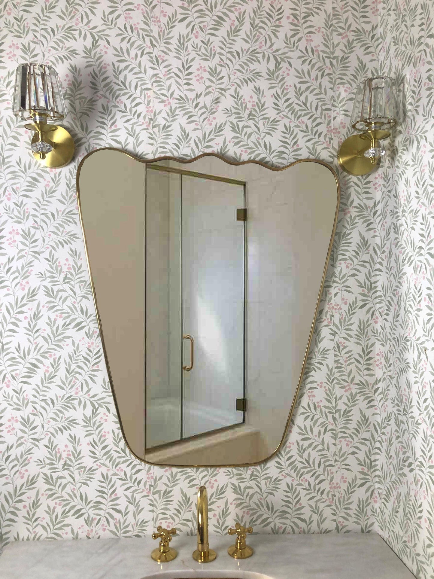 Bathroom mirror with gold fixtures and floral wallpaper.