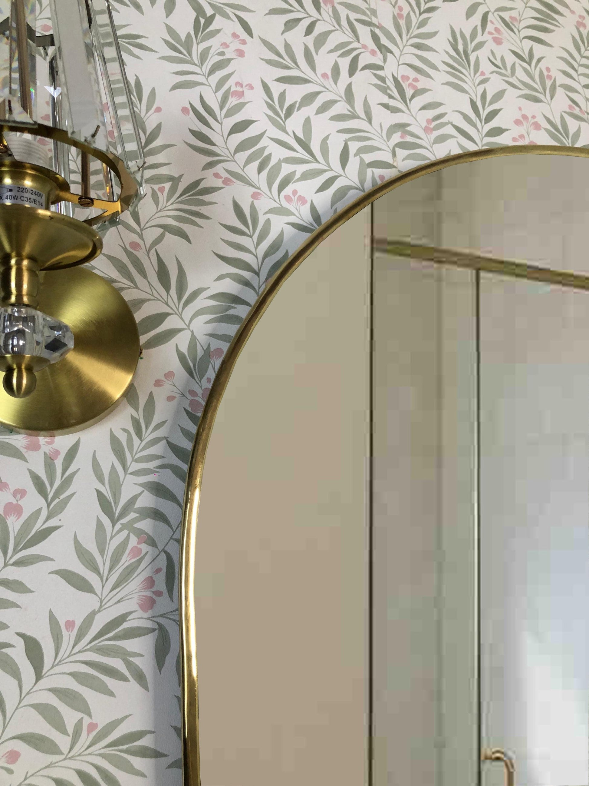 Brass arch mirror with crystal wall sconce on patterned wall.