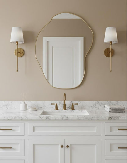 Asymmetrical brass bathroom mirror with marble countertop and sconces