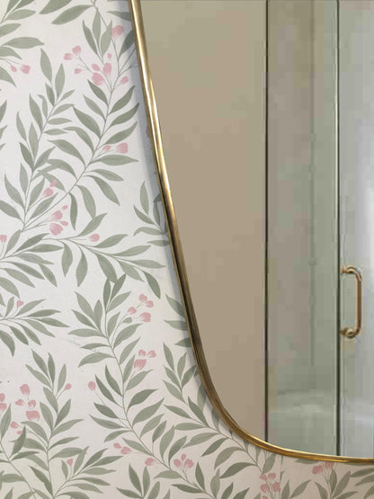 Lower corner detail of brass-framed mirror with leafy wallpaper.