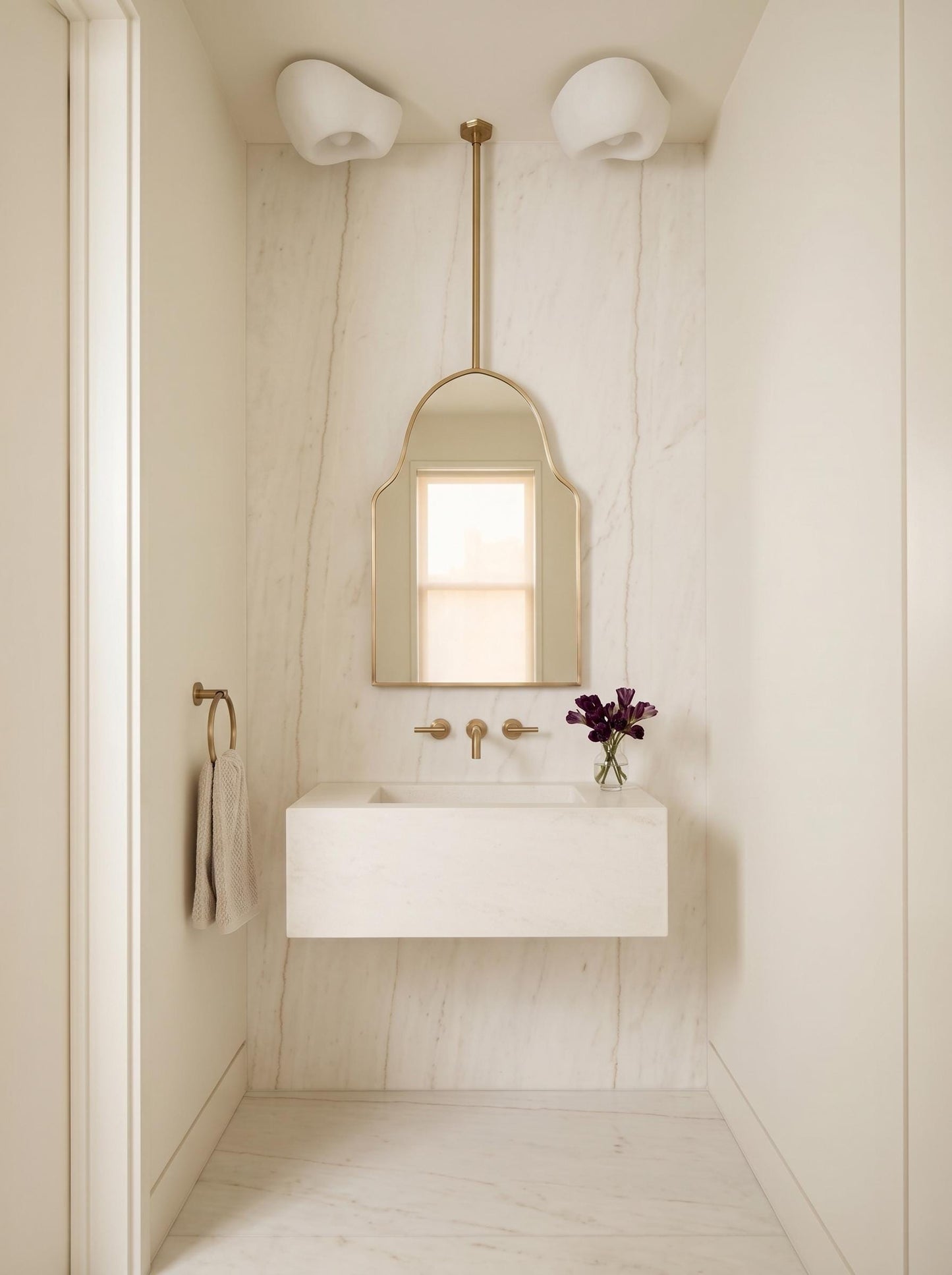 Suspended brass arch mirror above floating white vanity