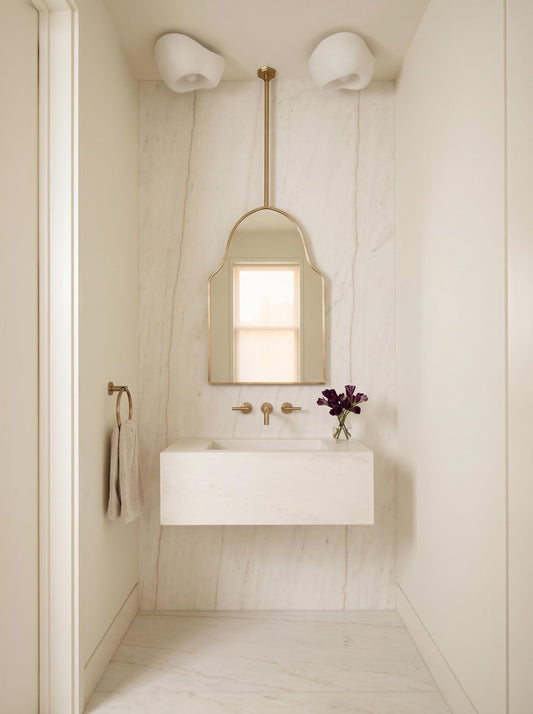 Suspended brass arch mirror above floating white vanity