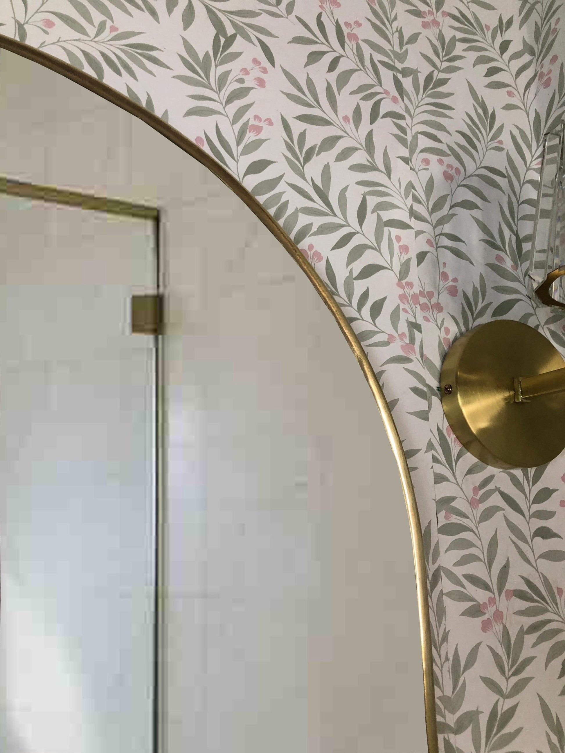 Upper corner of brass arch mirror with brass wall sconce.