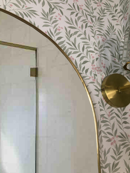 Upper corner of brass arch mirror with brass wall sconce.