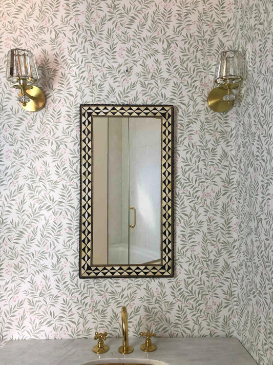Rectangular mirror with black and white geometric frame in a bathroom with floral wallpaper.