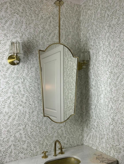 Suspended brass shield mirror above marble sink