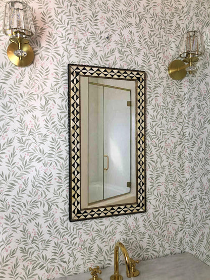 Bathroom view with brass fixtures, floral wallpaper, and geometric framed mirror.
