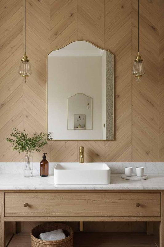 Arched brass framed mirror above vanity with white marble counter, wood panel walls, and pendant lights