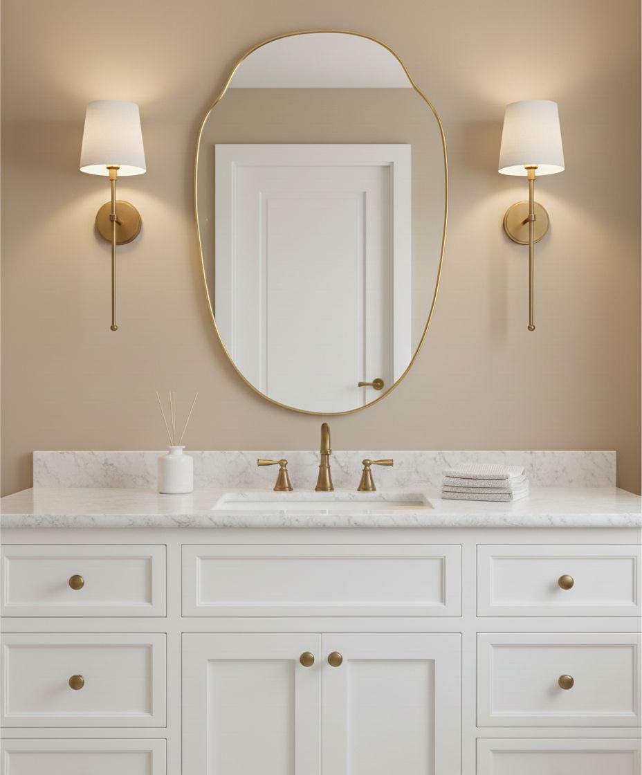 Modern irregular oval brass vanity mirror above white bathroom sink