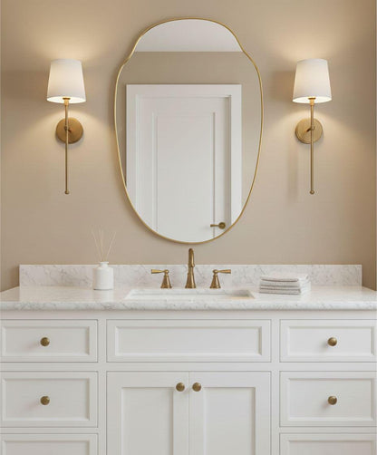 Modern irregular oval brass vanity mirror above white bathroom sink