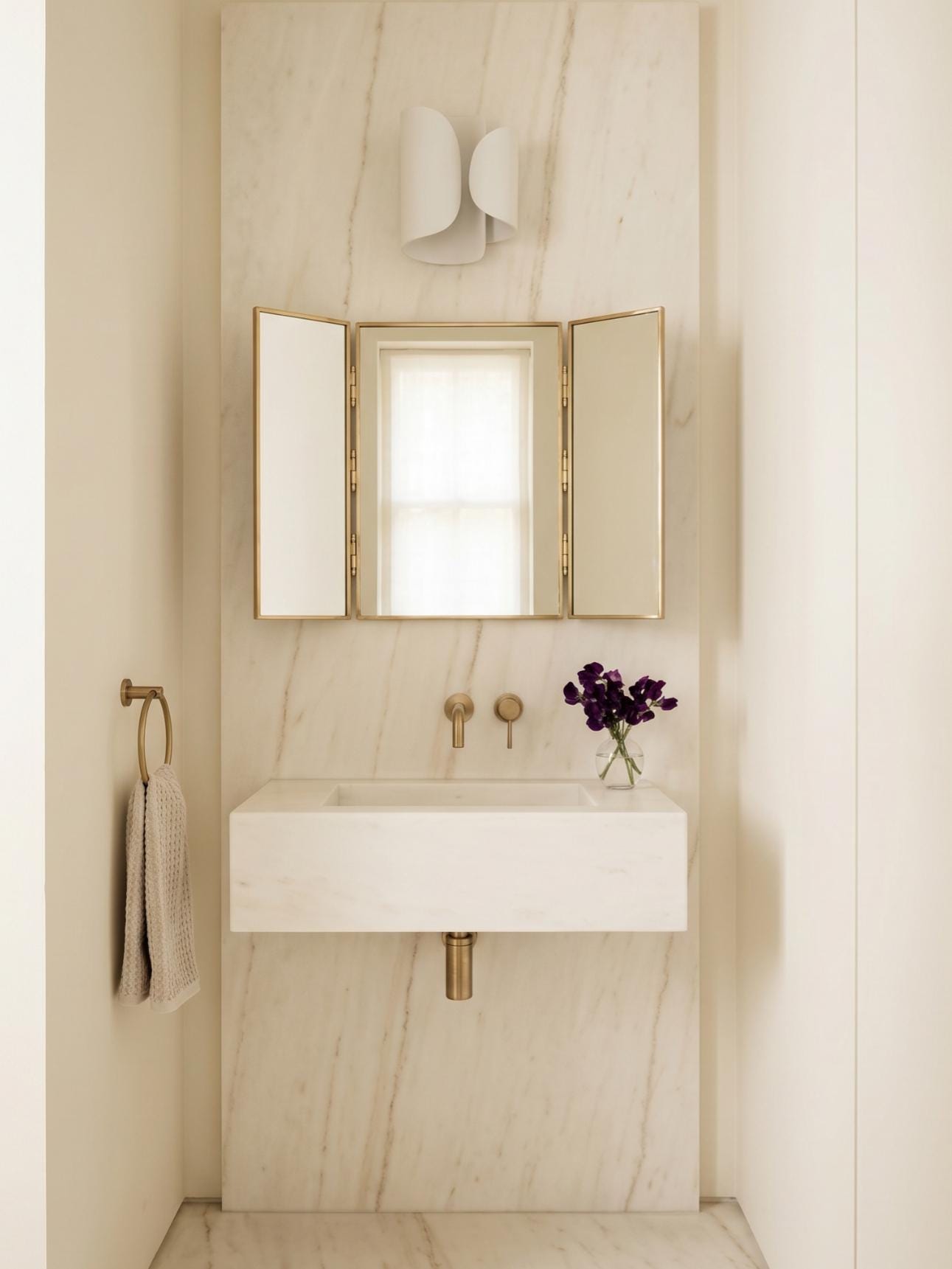 Brass trifold mirror above marble wall-mounted sink