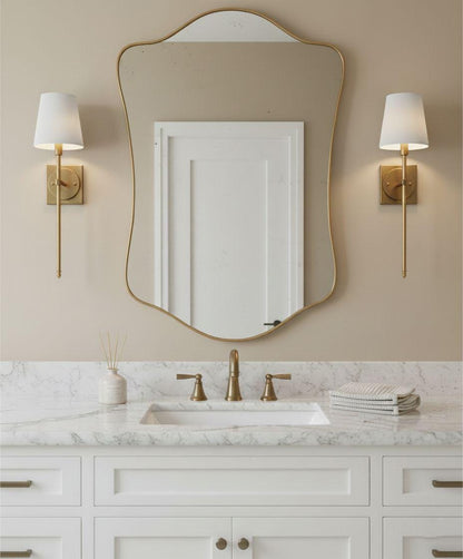 Curved irregular brass bathroom mirror above white vanity