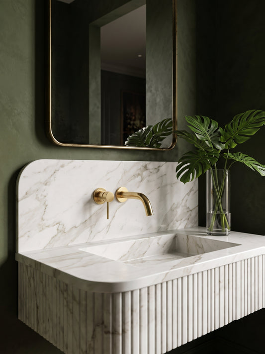 Minimalist solid brass wall-mounted faucet with single lever above a white marble fluted vanity in a luxury green bathroom.