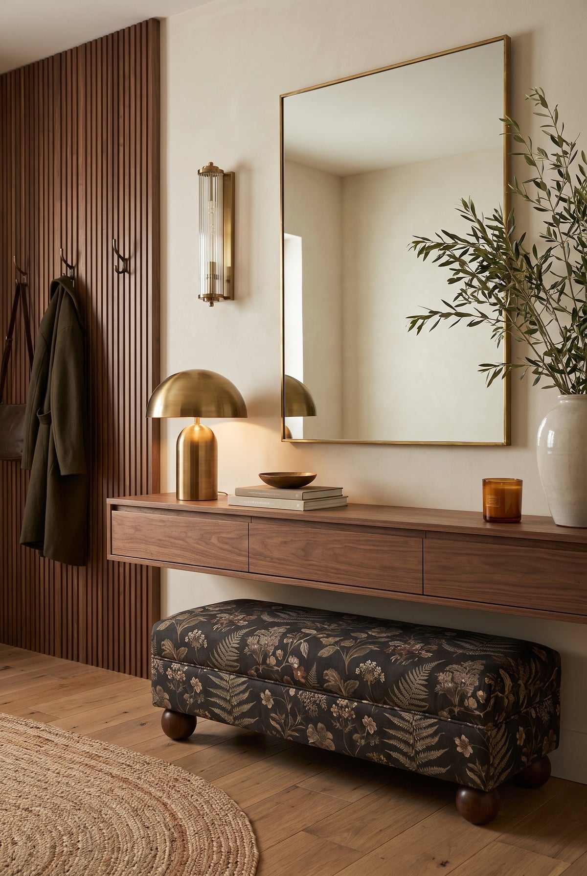 Large rectangular brass mirror above a walnut console with a brass dome lamp and botanical upholstered bench.