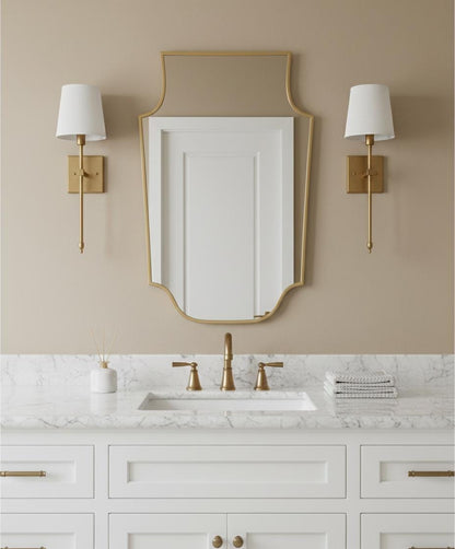 Shield-shaped brass mirror above marble bathroom vanity
