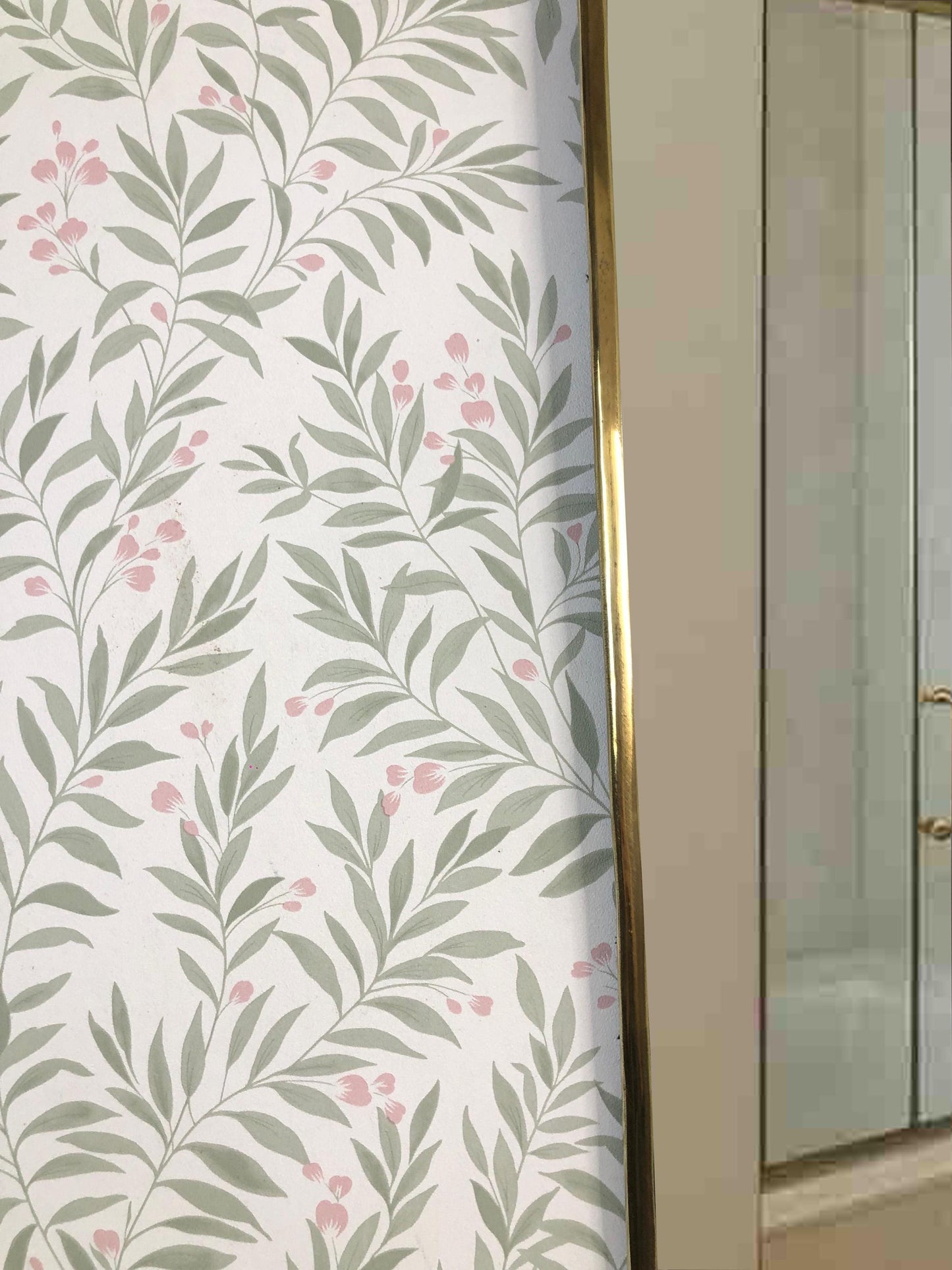 Close-up of brass mirror frame next to leafy wallpaper.
