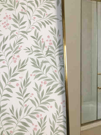 Close-up of brass mirror frame next to leafy wallpaper.