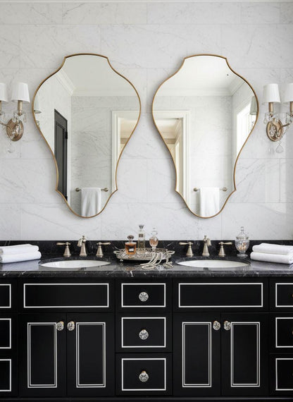Pair of asymmetrical brass vanity mirrors in marble bathroom