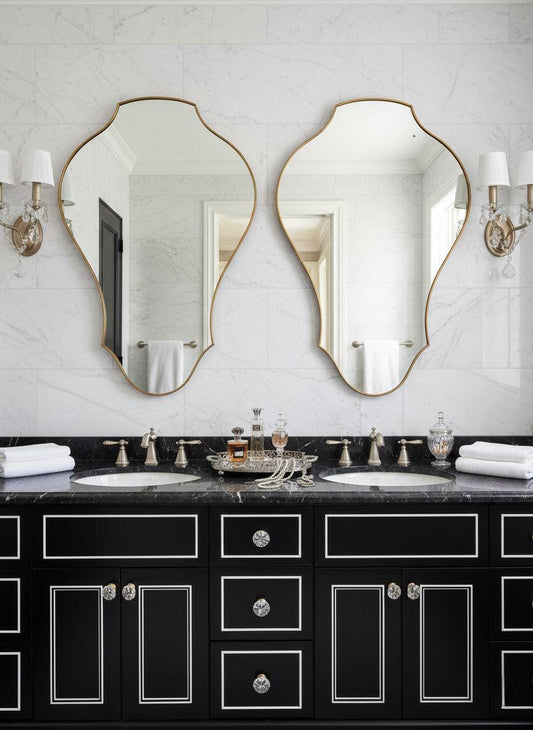Pair of asymmetrical brass vanity mirrors in marble bathroom