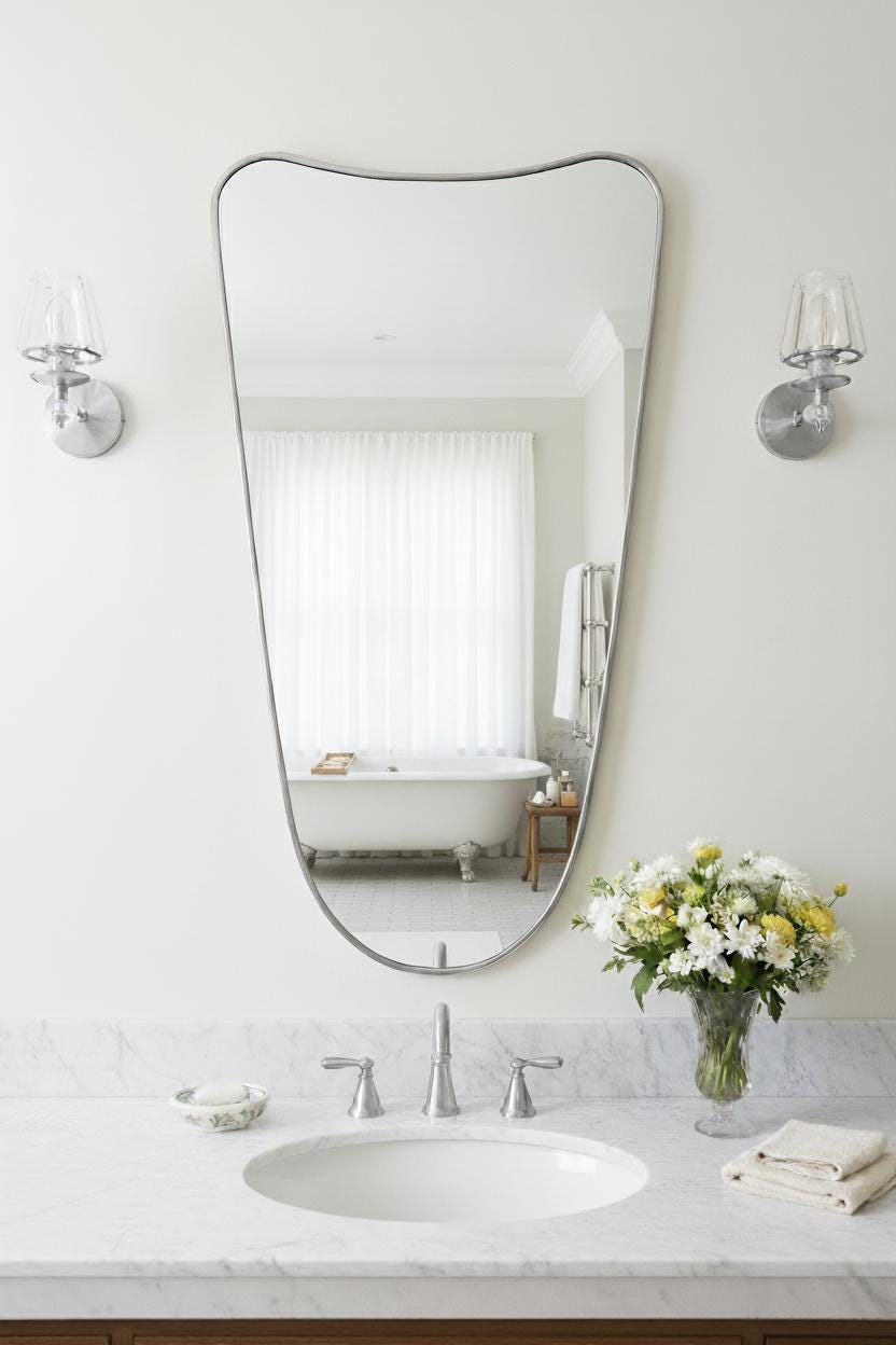 Silver curved mirror above a marble sink in a bright bathroom.