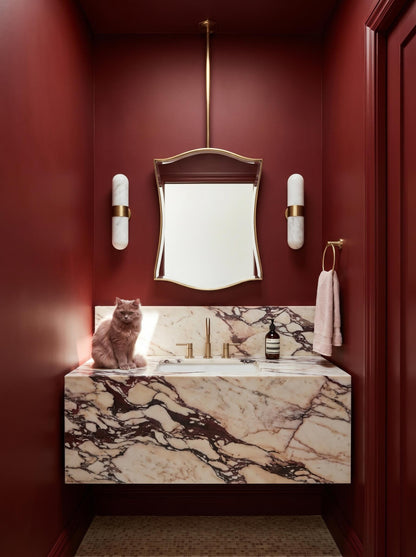 Curved brass hanging mirror in deep red luxury powder room